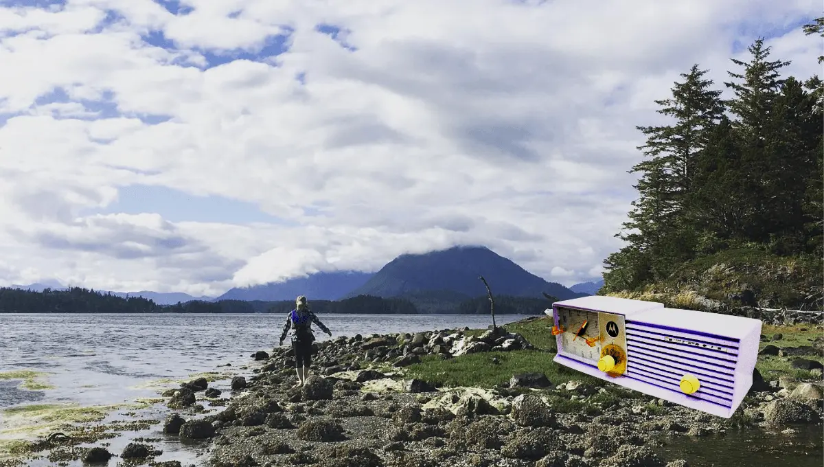 Stacey standing on a river shore, surrounded by Canadian woods with mountains going into the clouds in the background.